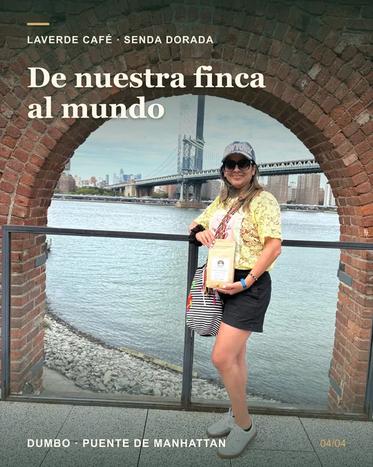 A woman holding a Senda Dorada coffee bag under a brick arch in DUMBO; Spanish caption: From our farm to the world.